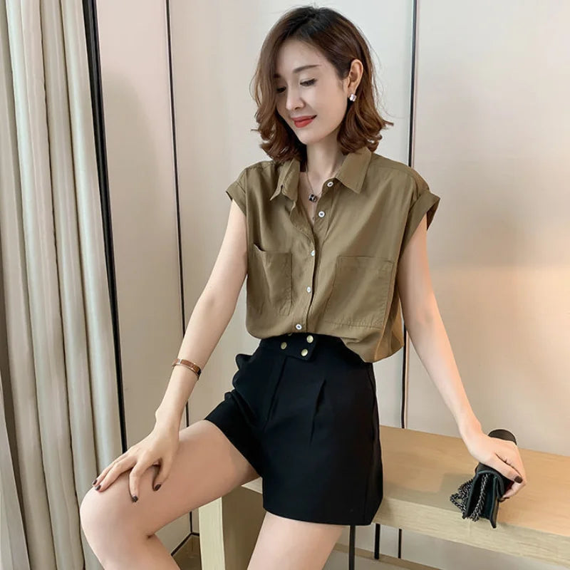 Camisa feminina sem manga com bolsos frontais e botões, em tom neutro, combinada com short preto de cintura alta.